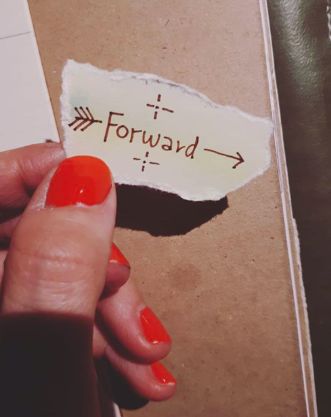 En papperslapp det står Forward på hållen av fingrar med rött nagellack, en symbol för Karolina Eleonoras healing arbete med Emotion Code vilken hon är välmeriterad och eftersökt för.